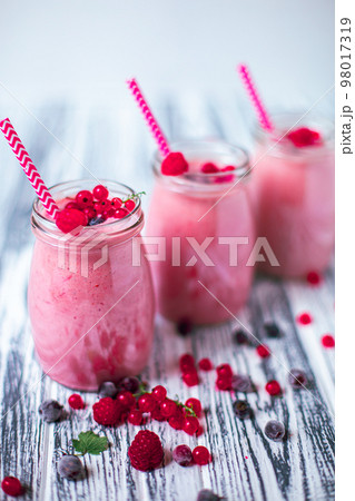 Front view of three berries milkshakes in glasses jars with ingredients on wooden table Front view of three berries milkshakes in glasses jars with ingredients on wooden table 98017319