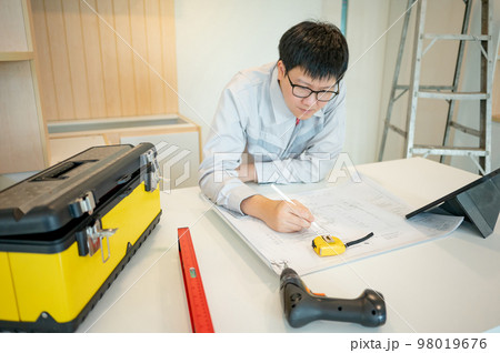 Asian male Interior worker working with architectural drawing Asian male Interior worker working with architectural drawing 98019676