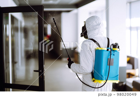 Disinfecting of office to prevent COVID-19, Man in protective hazmat suit with spray chemicals. Disinfecting of office to prevent COVID-19, Man in protective hazmat suit with spray chemicals. 98020049