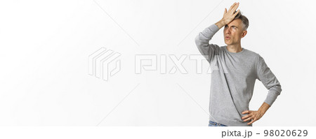 Image of frustrated and distressed middle-aged man, making facepalm and exhaling disappointed, standing over white background Image of frustrated and distressed middle-aged man, making facepalm and exhaling disappointed, standing over white background 98020629
