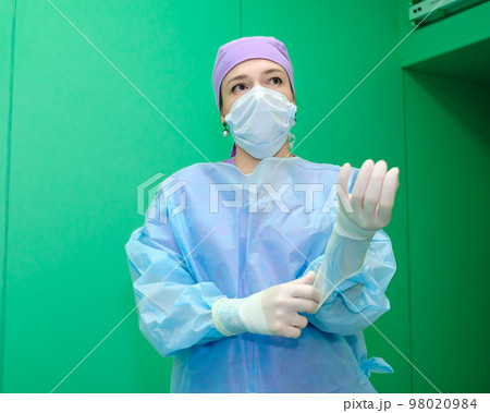 A female doctor in a surgical uniform pulls sterile gloves on her hand. A female doctor in a surgical uniform pulls sterile gloves on her hand. 98020984