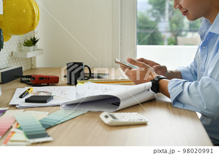 Architects man using mobile phone, working on design of a construction plan at creative workplace Architects man using mobile phone, working on design of a construction plan at creative workplace 98020991