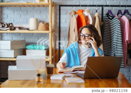 Smiling woman takes notes of orders from with laptop. Dropshipping owner works. Smiling woman takes notes of orders from with laptop. Dropshipping owner works. 98021156