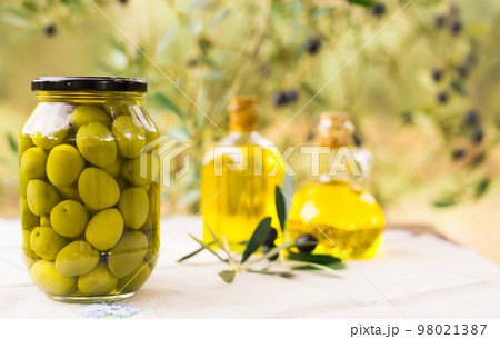 canned olives in a glass jar, oil and olives on the table against the background of the olive garden 98021387