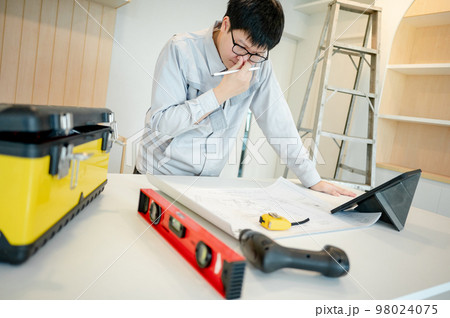Asian male Interior worker working with architectural drawing Asian male Interior worker working with architectural drawing 98024075