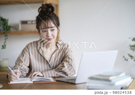 ノートパソコンの画面を見ながらメモをとる若い女性 98024538