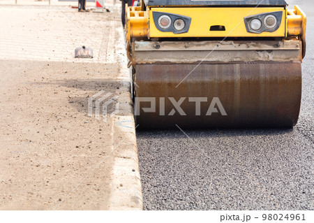 The metal wheel of the vibration rink rammed fresh asphalt on the road. The metal wheel of the vibration rink rammed fresh asphalt on the road. 98024961