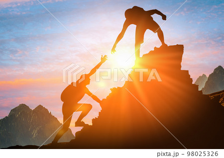 Man is giving helping hand. Silhouettes of people climbing on mountain at sunset. Help and assistance concept. Silhouettes of two people climbing on mountain and helping. Man is giving helping hand. Silhouettes of people climbing on mountain at sunset. Help and assistance concept. Silhouettes of two people climbing on mountain and helping. 98025326