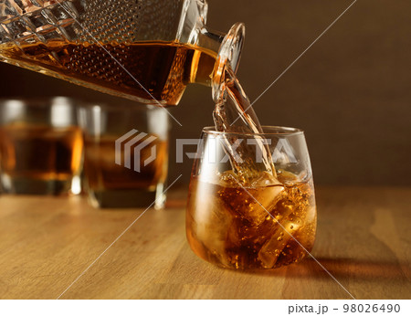 Whiskey is poured into a dammed glass with ice. Whiskey is poured into a dammed glass with ice. 98026490