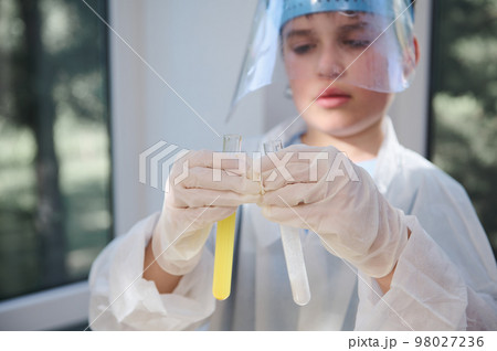 Details: gloved hands of a blurred smart teen schoolboy, wearing protective lab wear, holding test tubes with chemicals and reagents, conducting experiment in the school chemistry laboratory Details: gloved hands of a blurred smart teen schoolboy, wearing protective lab wear, holding test tubes with chemicals and reagents, conducting experiment in the school chemistry laboratory 98027236