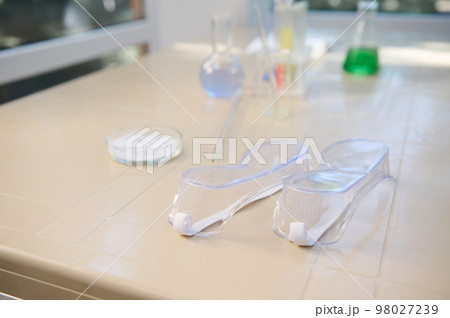 Selective focus on protective goggles - safety lab eyeglasses, eyewear on a plastic table, against the background of laboratory glassware 98027239