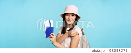Happy asian girl tourist got vaccinated to travel abroad, showing arm with plaster and passport with two tickets, booking tour, travelling during pandemic, blue background Happy asian girl tourist got vaccinated to travel abroad, showing arm with plaster and passport with two tickets, booking tour, travelling during pandemic, blue background 98033271