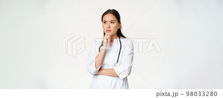 Image of serious doctor, female healthcare worker thinking, looking aside with concerned, frowning face expression, white background Image of serious doctor, female healthcare worker thinking, looking aside with concerned, frowning face expression, white background 98033280