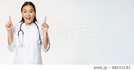 Excited smiling nurse, female doctor in medical uniform pointing up, showing promo sale, healthcare clinic discount, standing over white background Excited smiling nurse, female doctor in medical uniform pointing up, showing promo sale, healthcare clinic discount, standing over white background 98033282