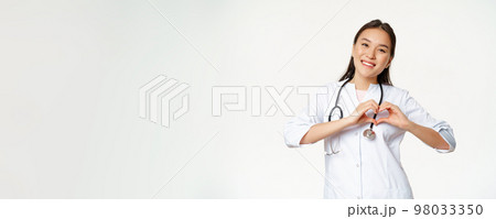 Smiling asian female doctor care for her patients, shows heart gesture and looking happy, standing in medical clinic uniform, white background Smiling asian female doctor care for her patients, shows heart gesture and looking happy, standing in medical clinic uniform, white background 98033350