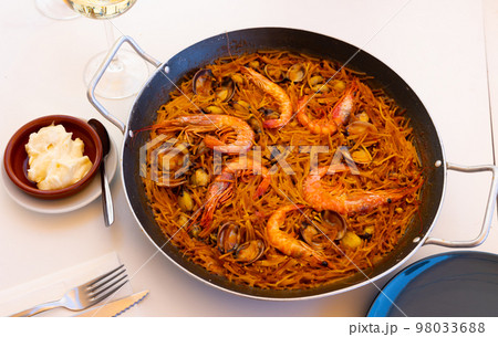 Seafood fideua with shrimps, squid and clams in paellera with allioli 98033688
