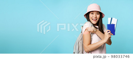 Enthusiastic korean woman shows her vaccinated arm, passport tickets. Tourist looks happy after covid-19 vaccine shot, travelling abroad, tourism concept 98033746
