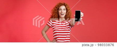 Cheerful attractive charismatic european redhead girl curly hairstyle show smartphone screen smiling happily promote app advice recommend good application social media page red background Cheerful attractive charismatic european redhead girl curly hairstyle show smartphone screen smiling happily promote app advice recommend good application social media page red background 98033876