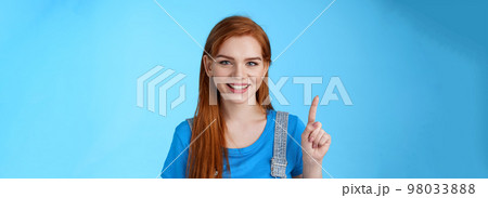 Close-up cute tender redhead european female make order, show number one first, smiling friendly carefree, extend finger, pointing up, counting stand blue background joyful Close-up cute tender redhead european female make order, show number one first, smiling friendly carefree, extend finger, pointing up, counting stand blue background joyful 98033888