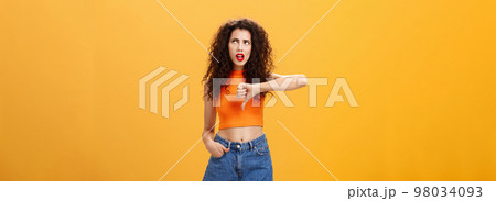 Party for losers I am out. Dissatisfied attractive popular girl with curly hairstyle in red lipstick and cropped top rolling eyes up from irritation and dislike showing thumb down over orange wall Party for losers I am out. Dissatisfied attractive popular girl with curly hairstyle in red lipstick and cropped top rolling eyes up from irritation and dislike showing thumb down over orange wall 98034093