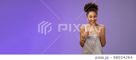 Good-looking daring african-american woman elegant silver evening dress agree help show thumbs up approval like gesture smiling broadly recommend great service think outfit suits her 98034264