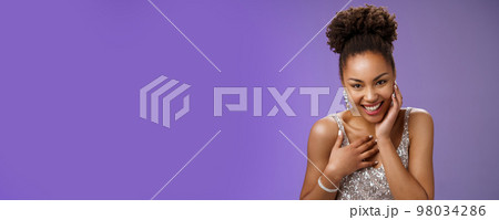Close-up flirty cheeky young stylish african american woman attend luxurious party in silver dress giggling receive compliment smiling gladly touch chest grateful standing pleased blue background 98034286