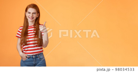 Cheerful friendly woman red natural hair clean skin, show thumb up, smiling approval, support perfect choice, like excellent performance, express positive opinion, acceptance, orange background 98034533