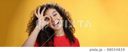 Hey I see you. Charismatic funny and playful cute tender girlfriend with curly hair showing okay or zero gesture over eye peeking at camera and smiling broadly, tilting head right over yellow wall Hey I see you. Charismatic funny and playful cute tender girlfriend with curly hair showing okay or zero gesture over eye peeking at camera and smiling broadly, tilting head right over yellow wall 98034839