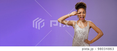 Charming lively african-american woman in glittering silver dress having fun smiling amused joyfully show victory peace gesture eye hold hand waist confident enthusiastic pose blue background Charming lively african-american woman in glittering silver dress having fun smiling amused joyfully show victory peace gesture eye hold hand waist confident enthusiastic pose blue background 98034863