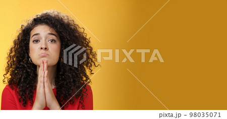 Please I beg you. Portrait of sad and cute curly-haired girl with angel eyes pouting holding hands in pray and looking hopeful at camera waiting for mercy asking apology, supplicating over yellow wall Please I beg you. Portrait of sad and cute curly-haired girl with angel eyes pouting holding hands in pray and looking hopeful at camera waiting for mercy asking apology, supplicating over yellow wall 98035071