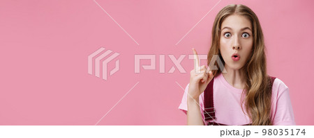 Close-up shot of creative emotive young cute female student with beautiful natural wavy hair raising index finger in eureka gesture folding lips while saying suggestion amazed and thrilled Close-up shot of creative emotive young cute female student with beautiful natural wavy hair raising index finger in eureka gesture folding lips while saying suggestion amazed and thrilled 98035174