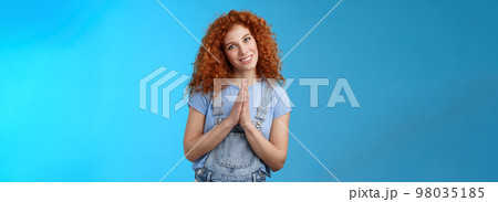 Girl acting like nun redhead cute curly female press palms together pray supplication gesture tilting head silly smiling innocent angel gaze pleading begging favour asking something blue background 98035185