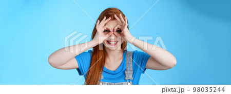 Playful cheerful redhead european woman, long nature red hairstyle, show okay finger glasses look through ok signs, smiling broadly funny grimace, stand blue background carefree enjoy summer Playful cheerful redhead european woman, long nature red hairstyle, show okay finger glasses look through ok signs, smiling broadly funny grimace, stand blue background carefree enjoy summer 98035244