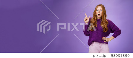Shocked girl in stupor drop jaw and pop eyes at camera from amazement of unexpected stunning copy space pointing at upper left corner looking impressed and astonished over purpe background 98035390
