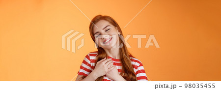 Close-up lovely caring tender redhead girlfriend feel love, close eyes smiling toothy silly grin, press palms heart, feel touched, daydreaming, have feelings, confess sympathy tasty food 98035455