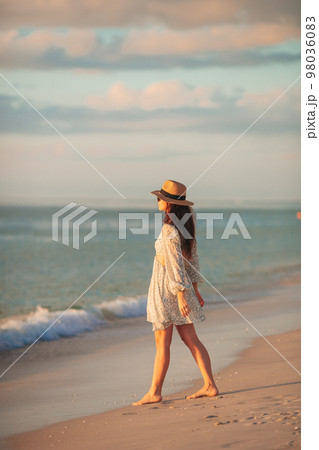Young beautiful woman at straw hat on the beach at sunset 98036083