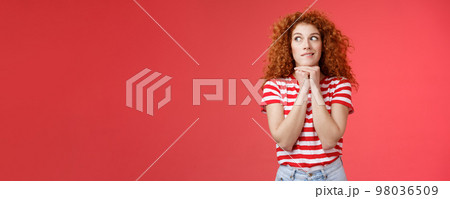 Cheerful intrigued redhead silly curly-haired woman smiling interested hold hands chin face-line imaging thinking about tasty burger look away desire have bite standing red background 98036509