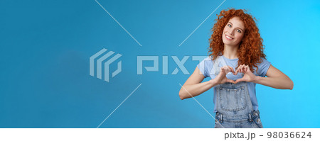 Caring tender lovely redhead girlfriend express sympathy tenderness gentle sympathy tilt head smiling broadly show heart love gesture chest cherish passionate romantic feelings, blue background 98036624