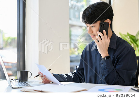 Side view of young businessman having a phone call with customer while working Side view of young businessman having a phone call with customer while working 98039054