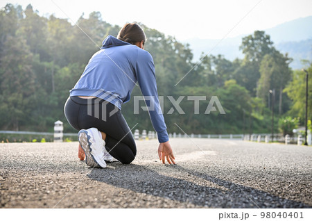 Athlete Asian female runner running start pose, preparing to run on the street. 98040401