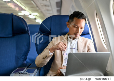 Professional and focused Asian businessman using a laptop computer during the flight. 98040641