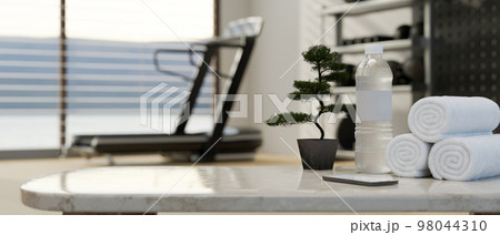 Copy space on table with bottle of water and towels over blurred background of fitness with treadmill Copy space on table with bottle of water and towels over blurred background of fitness with treadmill 98044310