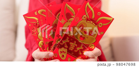 woman holding Chinese red envelope with golden rabbit and blessing word, money gift for happy Lunar New Year holiday. Chinese sentence means happiness, healthy, Lucky and Wealthy woman holding Chinese red envelope with golden rabbit and blessing word, money gift for happy Lunar New Year holiday. Chinese sentence means happiness, healthy, Lucky and Wealthy 98047698