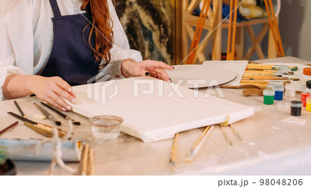 Painting hobby. Art class. Creative occupation. Unrecognizable female artist preparing blank white paper canvas at workplace with paintbrushes. Painting hobby. Art class. Creative occupation. Unrecognizable female artist preparing blank white paper canvas at workplace with paintbrushes. 98048206
