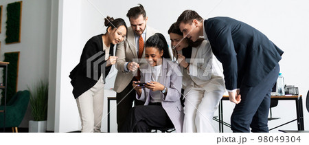 a team of colleagues in the office watches with interest how one employee plays a mobile phone a team of colleagues in the office watches with interest how one employee plays a mobile phone 98049304