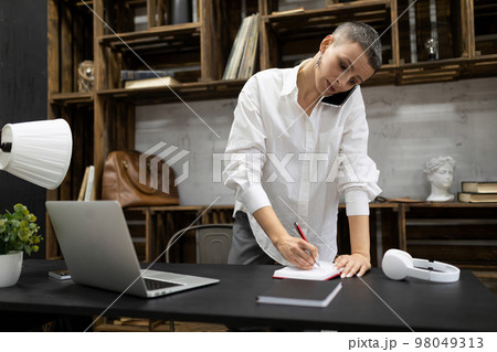 female office worker speaks on the phone and makes notes in a notebook while standing near the female office worker speaks on the phone and makes notes in a notebook while standing near the 98049313