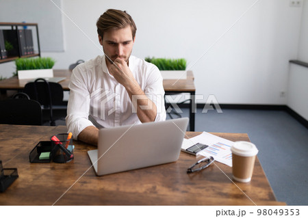 serious businessman in the office behind a laptop solves a complex business problem serious businessman in the office behind a laptop solves a complex business problem 98049353