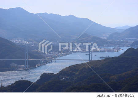 青空と山と海岸線の工場地帯と谷間の町並みの橋のかかる青い海面の船舶の行き交う海の見える風景 青空と山と海岸線の工場地帯と谷間の町並みの橋のかかる青い海面の船舶の行き交う海の見える風景 98049915
