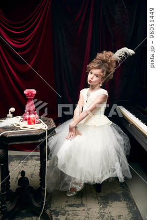 Portrait of cute little girl, child in image of medieval royal person in fabulous dress sitting at the piano and posing. Tenderness Portrait of cute little girl, child in image of medieval royal person in fabulous dress sitting at the piano and posing. Tenderness 98051449