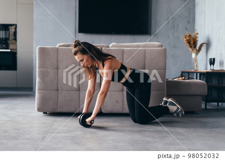 Fit woman working out with ab exercise wheel at home. Fit woman working out with ab exercise wheel at home. 98052032